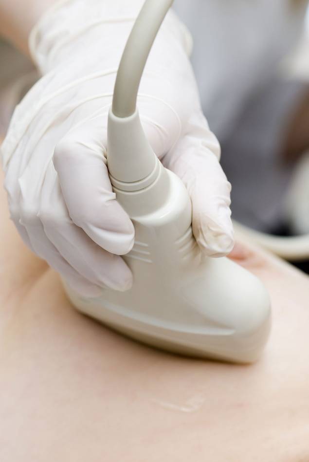 Nahaufnahme einer behandschuhten Hand, die während einer medizinischen Untersuchung eine Ultraschallsonde auf die Haut einer Person hält.